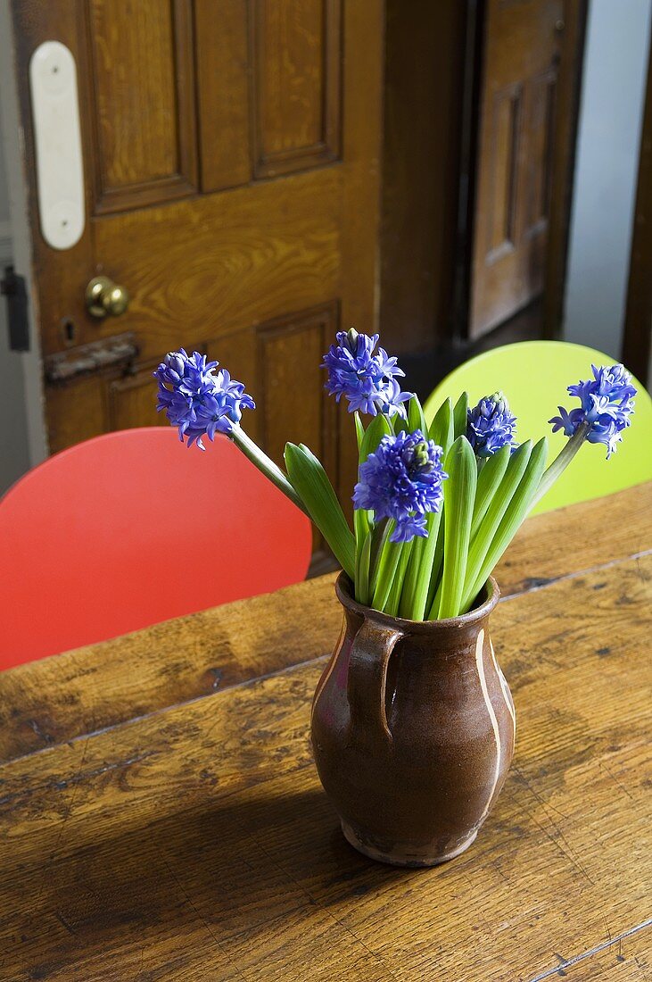 Blue hyacinths in a brown earthenware jug on an old wooden table