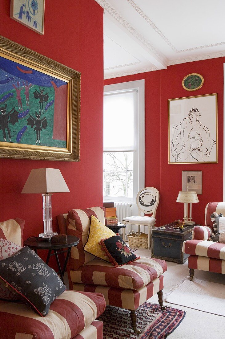 An open-plan living room with red walls and red and white striped armchairs in a villa