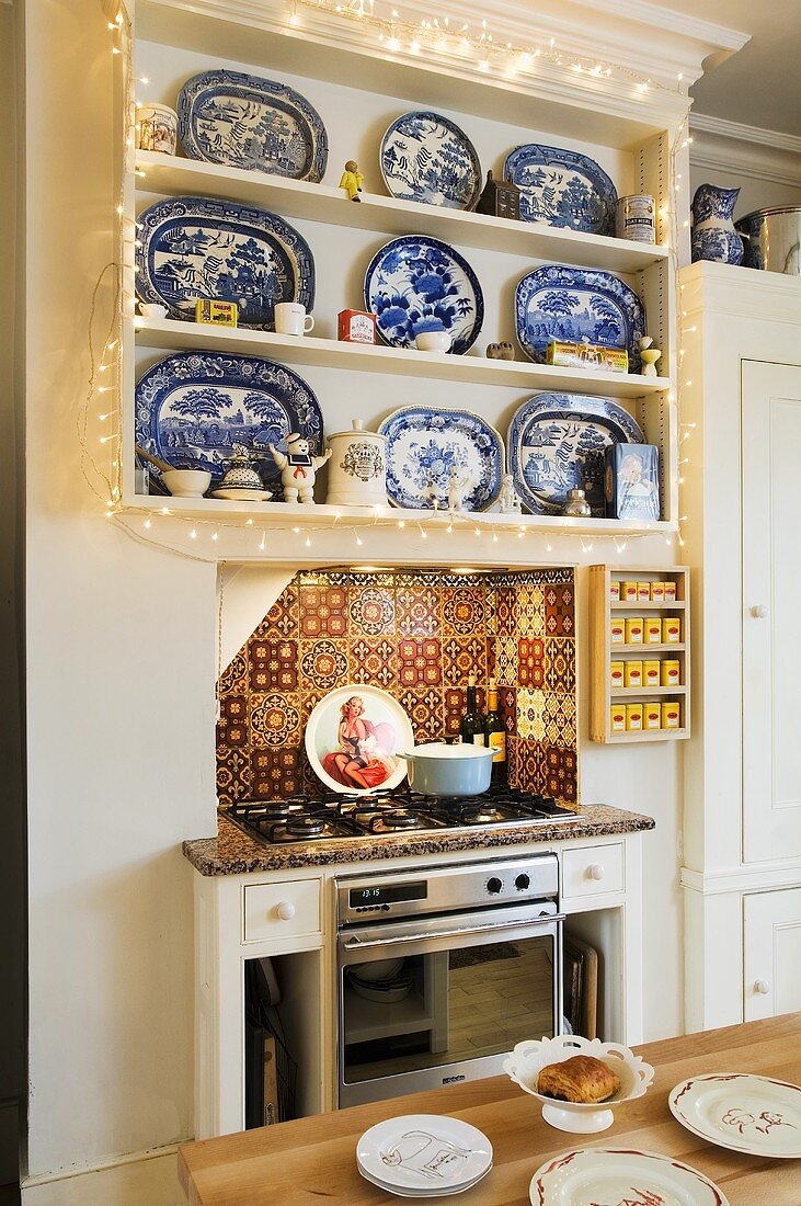 Lichterkette um Kücheneinbauregal mit weiss-blauen Schalen und orientalische Fliesen in der Nische mit Gasofen