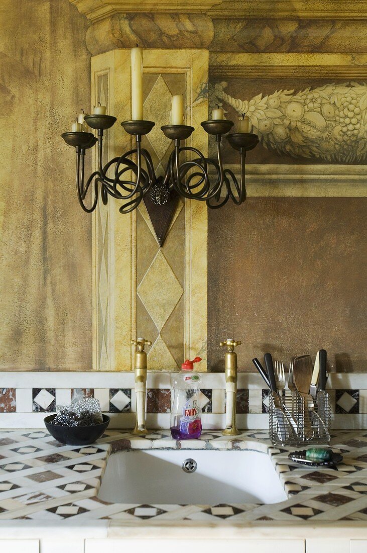 A metal chandelier on a painted wall and a basin let into a stone surface with a tiled pattern