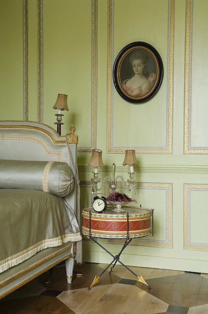 A bedroom with green wood panelling and gilded borders and an old drum being used as a bedside table