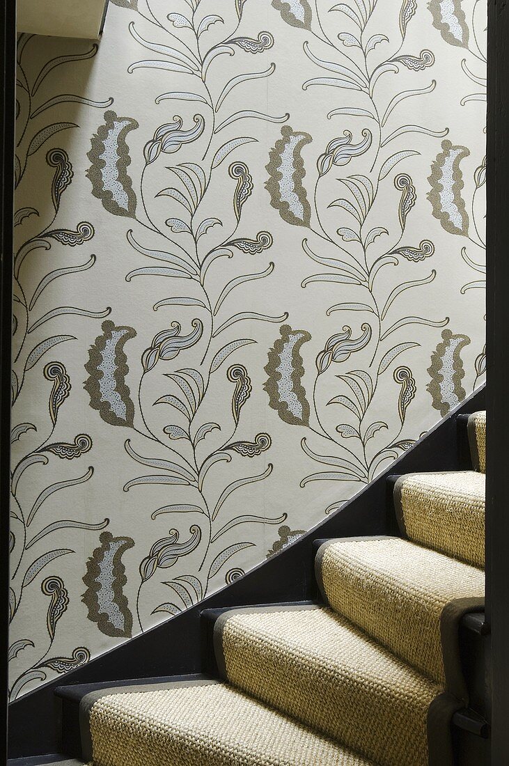 Treppenraum mit floraler Tapete auf Wand und Treppenaufgang mit hellem Teppichläufer