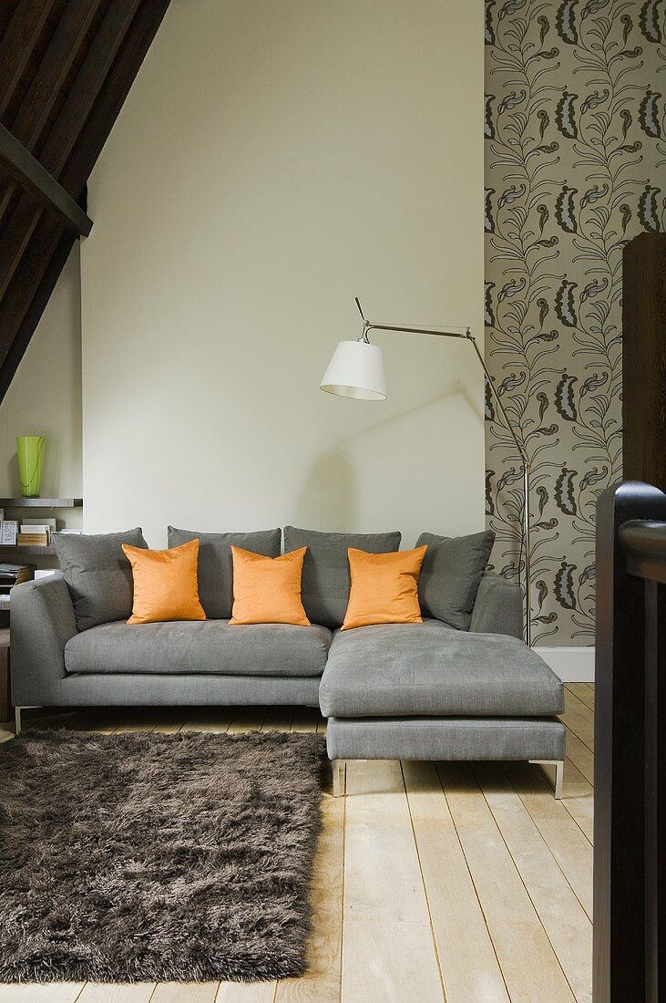 A grey sofa with orange cushions and a grey flokati rug under the slopping ceiling