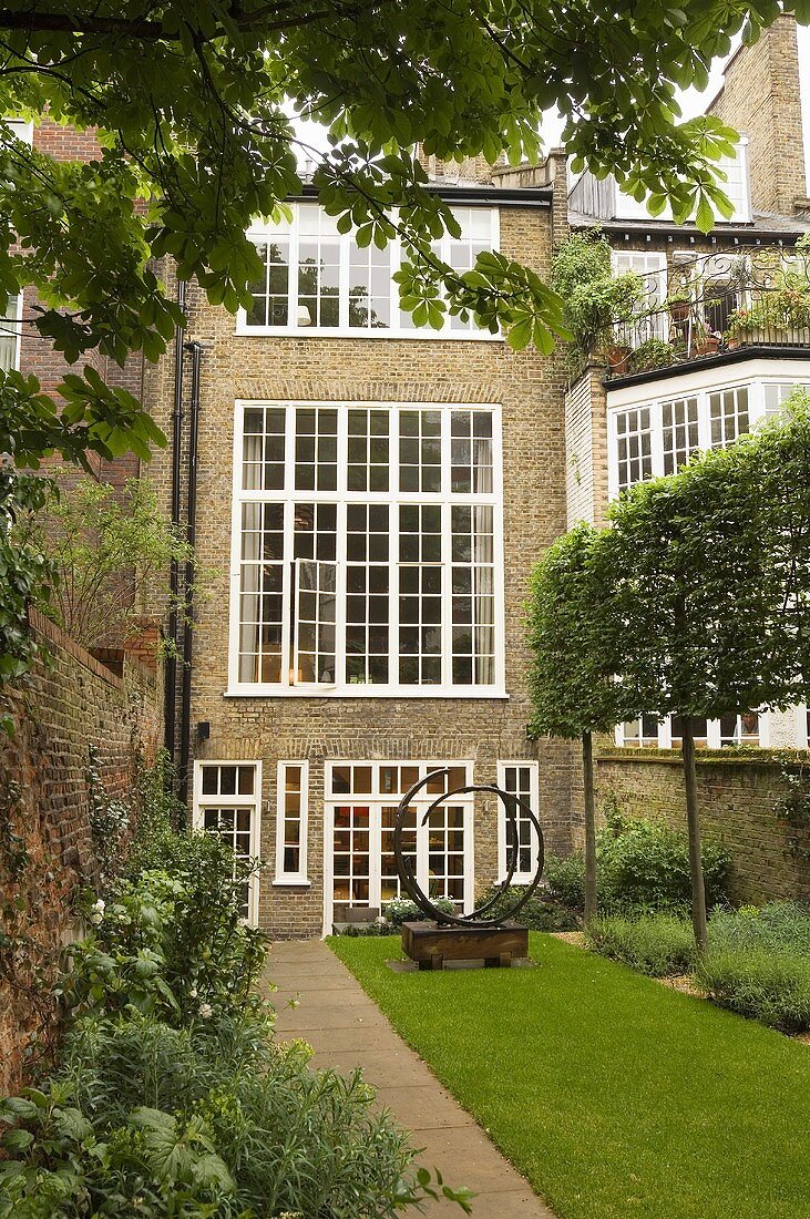 Englisches Wohnhaus mit weissen Sprossenfenstern und Skulptur im grünen Hinterhof