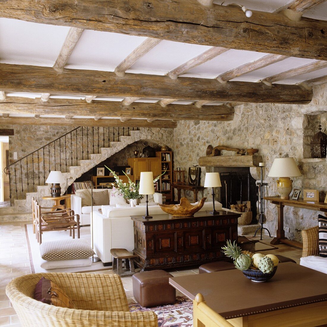 An open living room with a natural stone wall and a dining area under a rustic wooden beamed ceiling and view of a flight of stairs