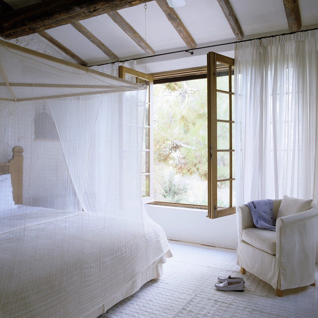 Weisser Schlafraum im Landhaus - Himmelbett mit leichtem Stoff vor geöffnetem Fenster