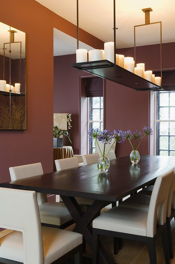 An elegant dining room with dark red walls and a hanging shelf with candles above a dark wooden table