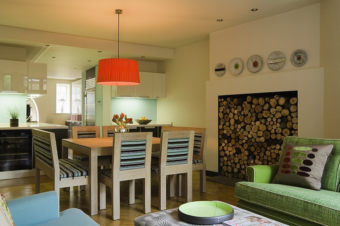 Offener Wohnraum mit orangen Deckenlampenschirm über Essbereich und Kamin mit Holzscheitenlager