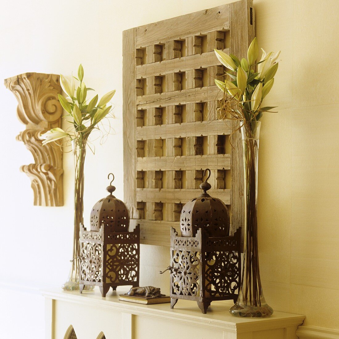 Oriental metal lanterns and lilies in glass vases in front of a rustic wooden latice