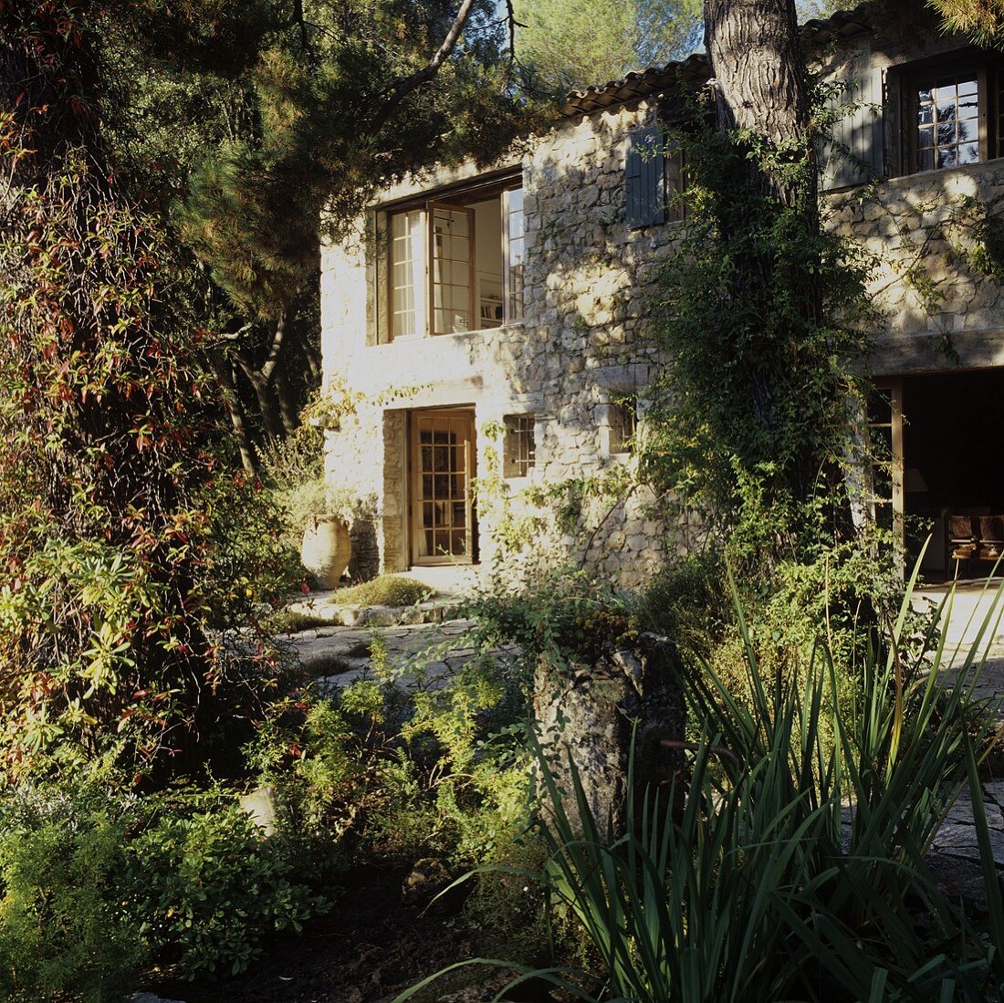 A Mediterranean country house with a natural stone facade, wooden transom windows and an overgrown garden