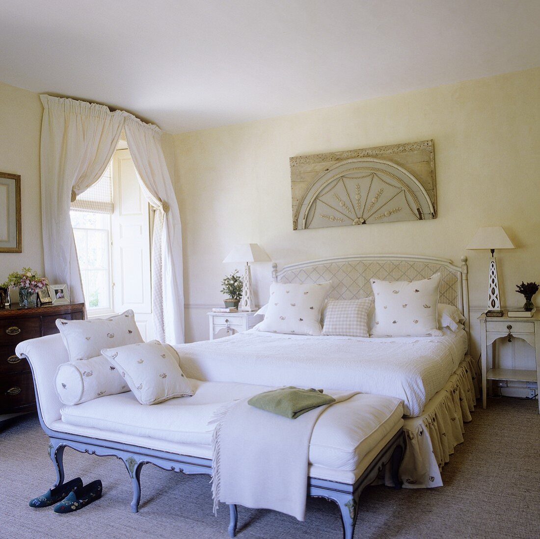 A light coloured bedroom in a country house with a chaise lounge in front of a double bed with white bedclothes