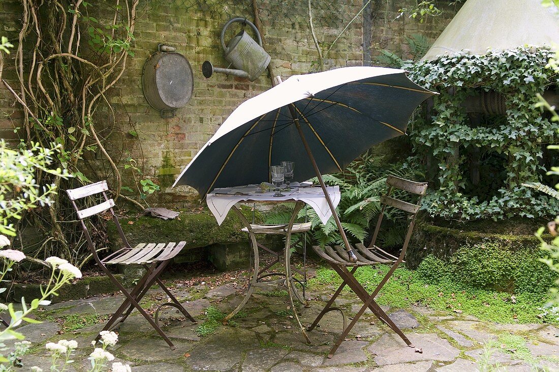 An old garden table with chairs and a parasol on a natural stone terrace in a rear courtyard