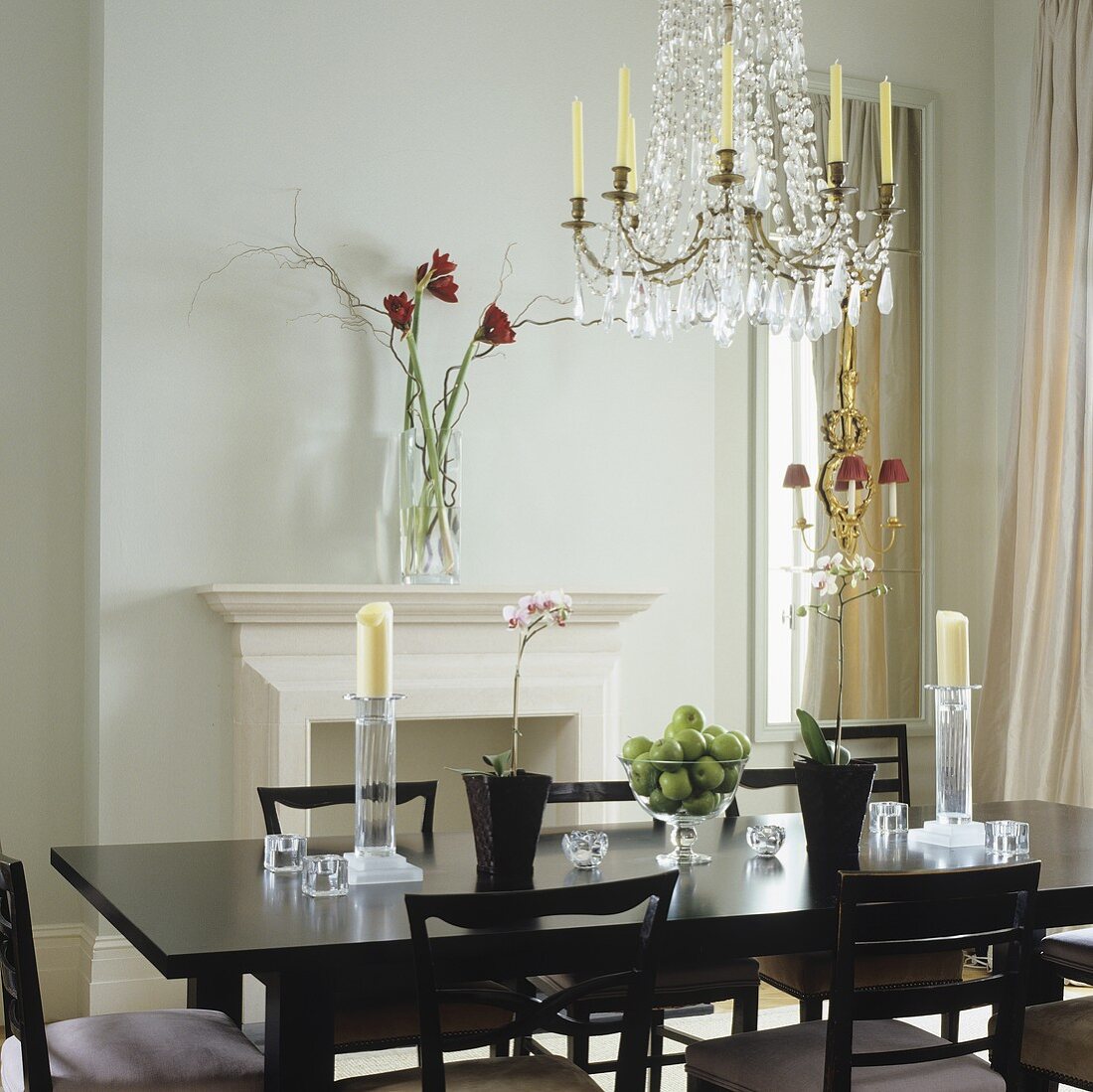 A dining room in an English apartment with a fireplace with an elegant black dining table and chairs with a crystal chandelier hanging from the ceiling