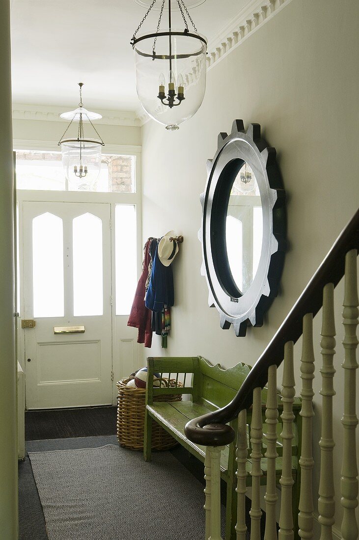 A hallway in a country-house with a mirror framed in a steering wheel and a green wooden bank