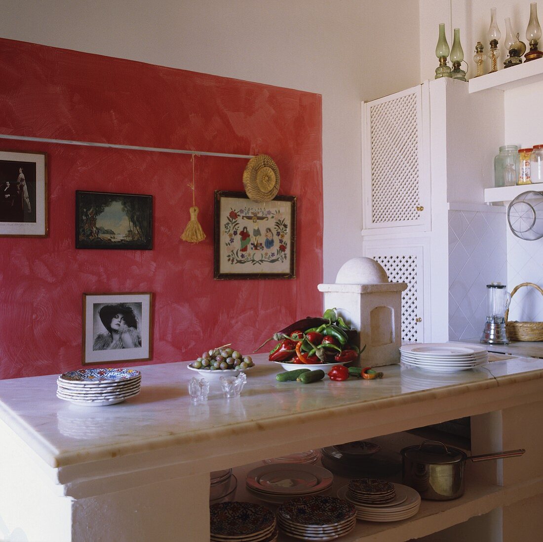 Mediterraner Küche - Marmorplatte auf weißem gemauerten Küchenblock vor roter Wand in Wischtechnik