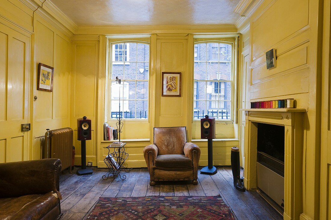 Gelbe Holzvertäfelung im Wohnraum mit Kamin und gemütlichem Ledersessel vor Fenster