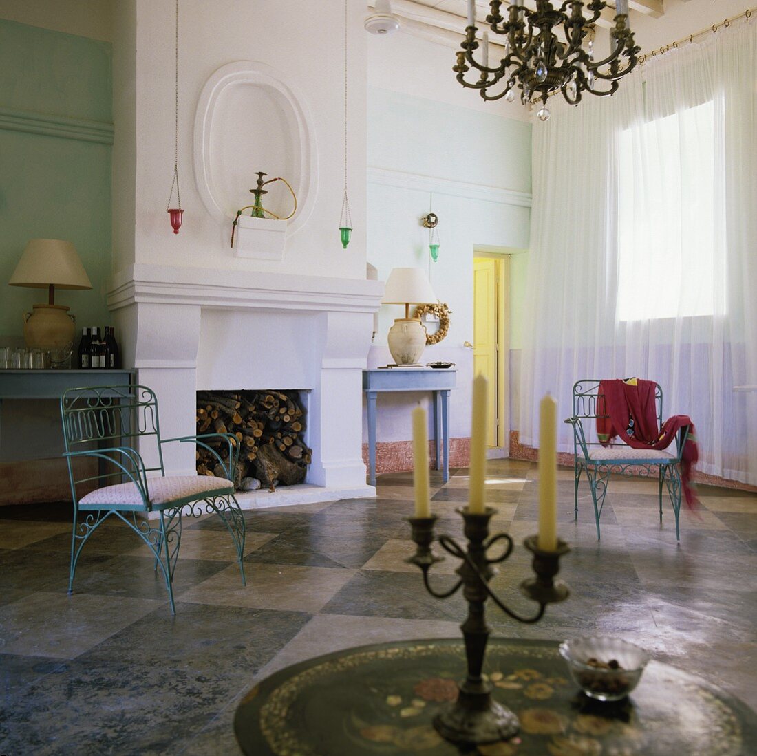 Kaminraum in Mediterraner Villa - antiker Kerzenständer auf Tisch und blaue Metallstühle auf Schachbrettmusterboden