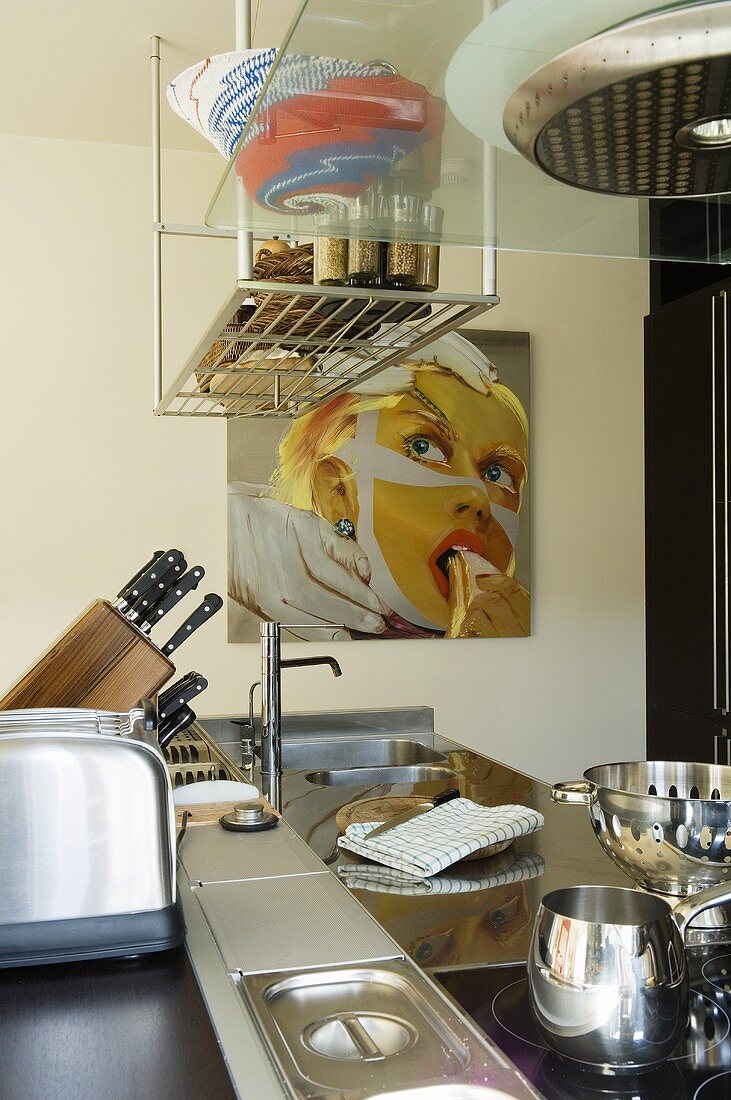 Kitchen utensils on a kitchen work surface with a stainless steel surface and a metal shelf hanging from the ceiling