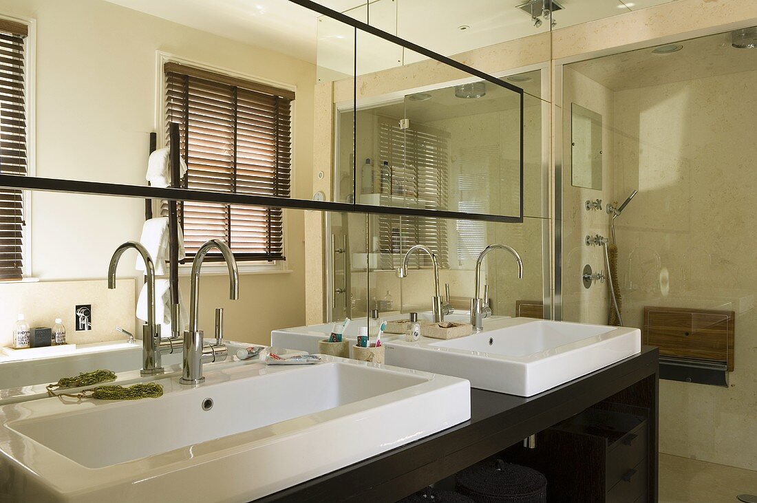A designer bathroom with a mirrored wall and a black washstand with two white basins