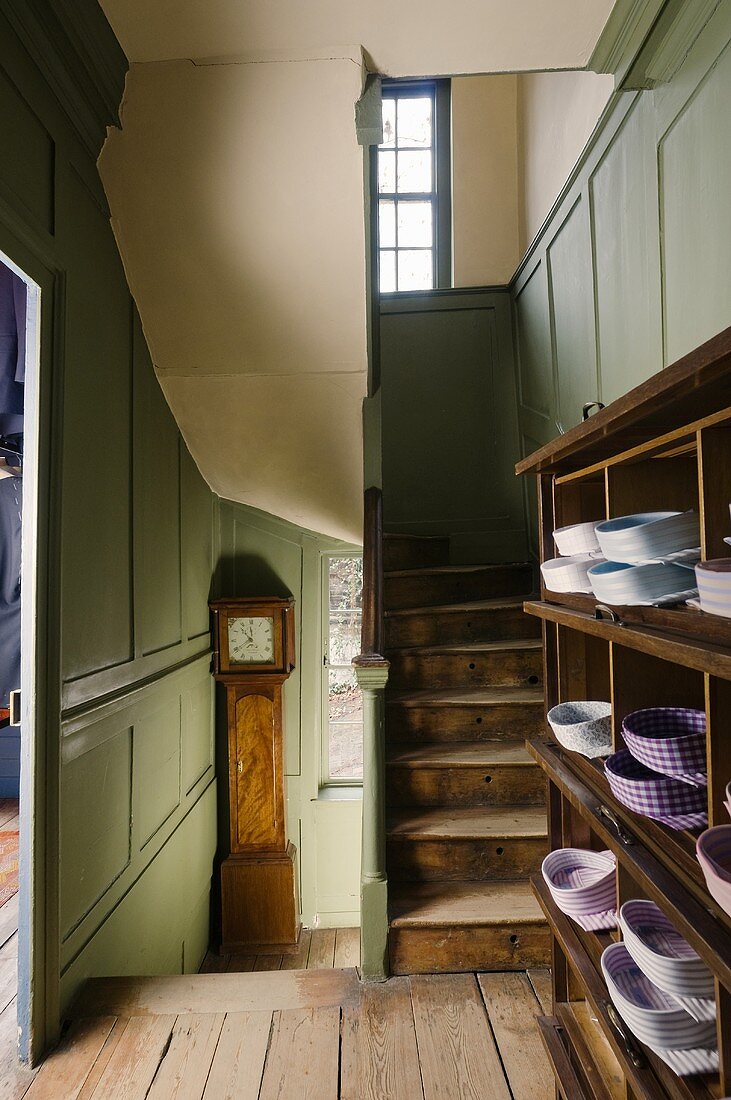 An old stairwell with a green wood panelled wall and an open cupboard on the landing filled with shirts
