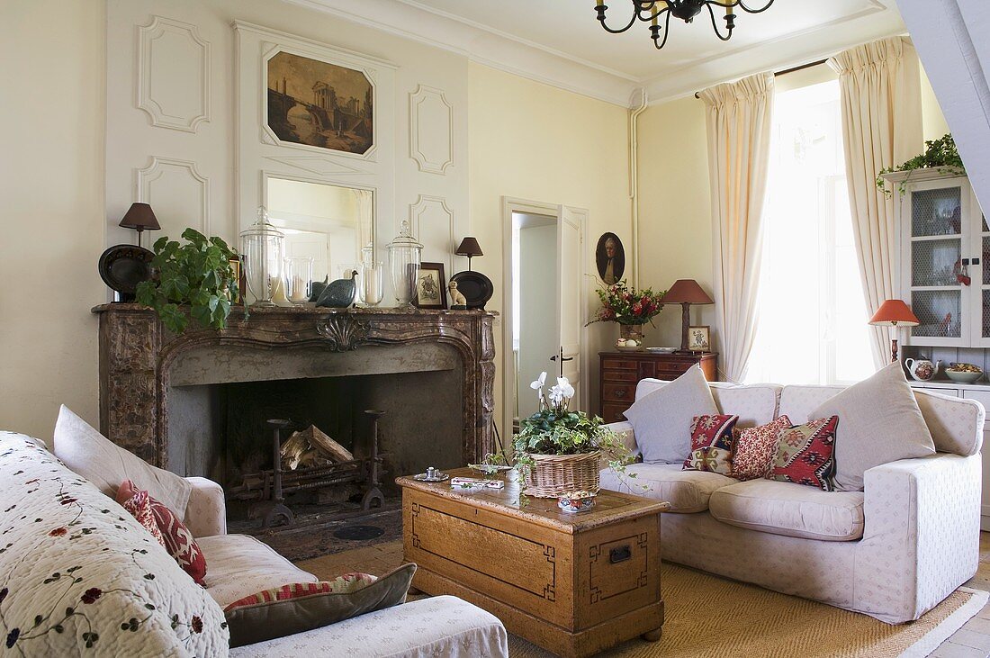 A wooden chest and a white sofa in front of a fireplace in the living room of a country house