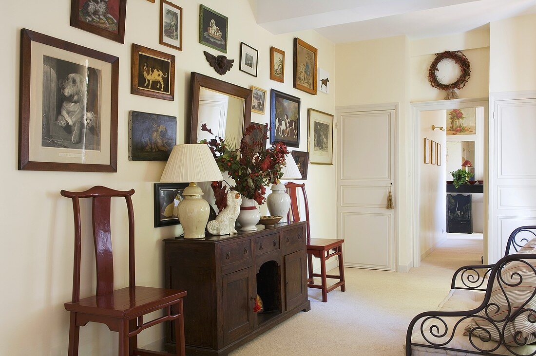A picture collection above a rustic sideboard with white table lamps in the hallway of a country house