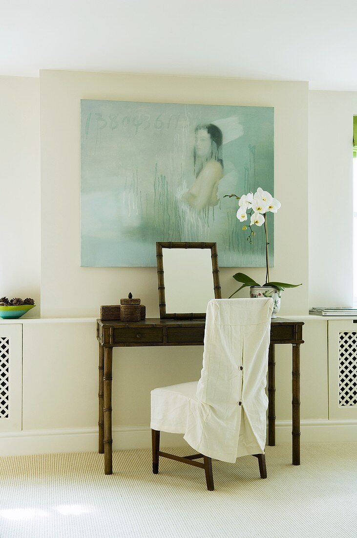 Bambustisch mit weißem Hussen Stuhl vor Wand mit Bild