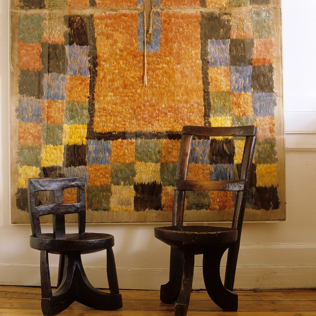 Wooden African chairs in front of a modern wall rug