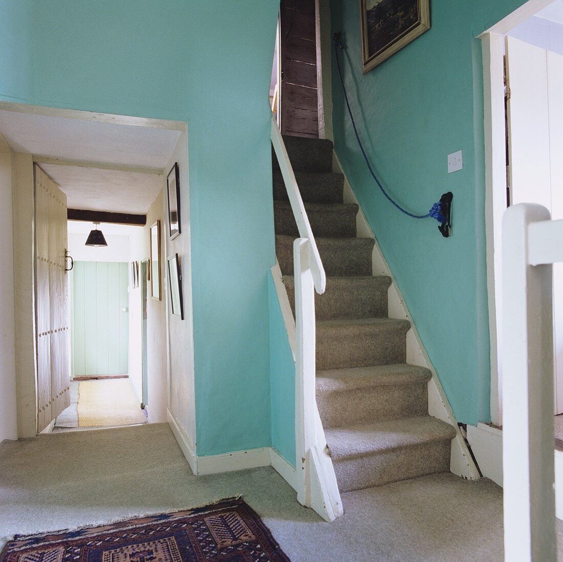 Schlichtes Treppenhaus mit türkisfarbenen Wänden und grauem Teppich auf Boden und Treppe mit Blick in den Flur