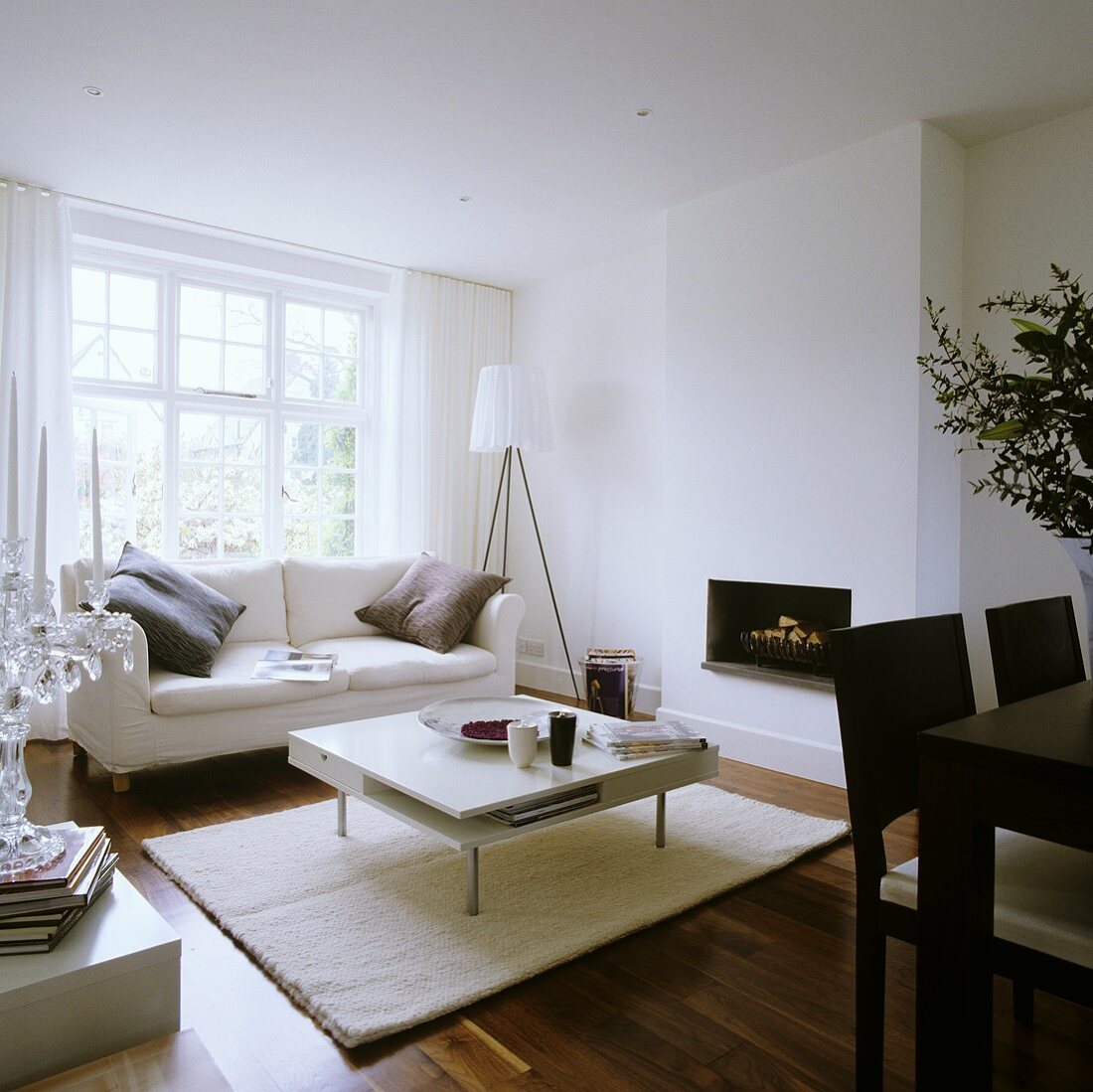 A white-painted designer living room with sofa in front of a window and a coffee table in front of a fireplace