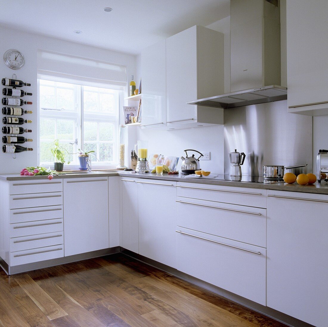 A corner of a white fitted kitchen with stainless steel handles and an integrated extractor hood