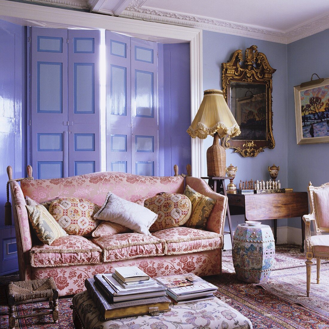 A shiny pink sofa and small items of furniture in a lilac-painted living room in a country house