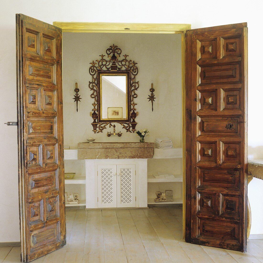 Offenstehende Holztüren mit Schnitzereien und Blick auf Steinbecken mit Spiegel im Goldrahmen