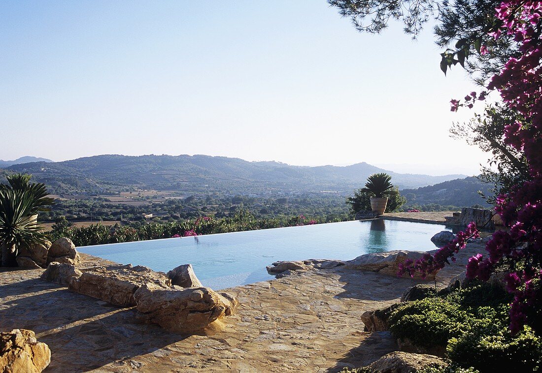 Natursteinboden und Felsblöcke vor Pool mit Ausblick auf die spanische Landschaft