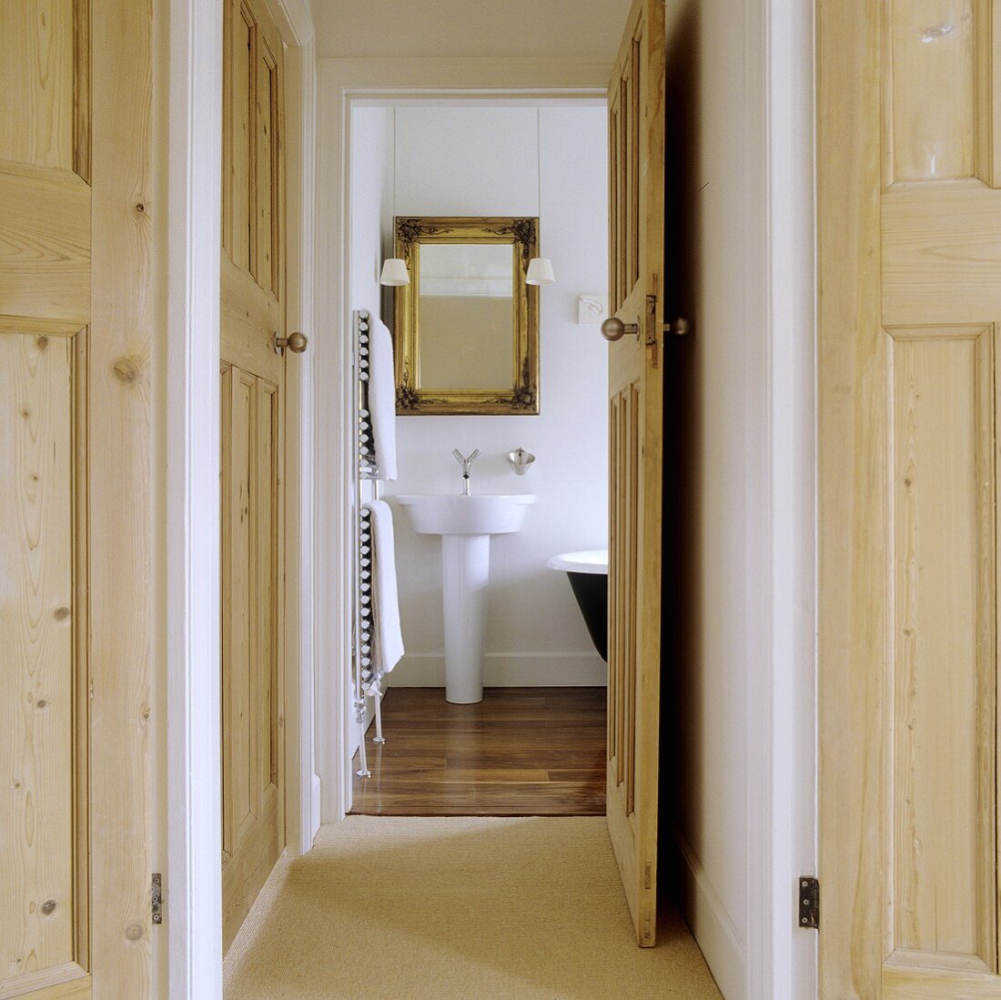 The hallway of an apartment with an open wooden door providing a view onto a designer wash basin and a golden-framed mirror
