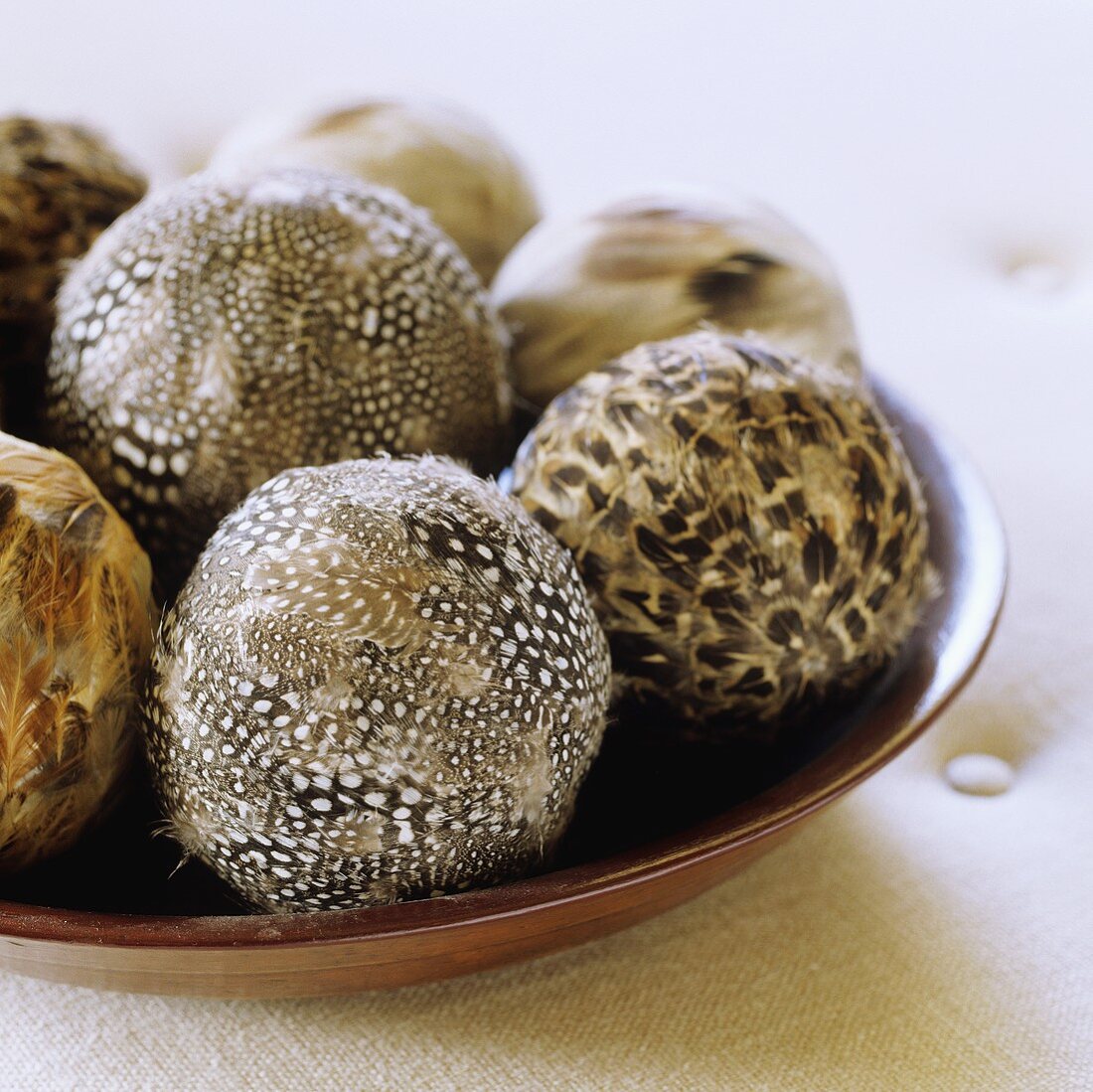 Brown and white patterned feathers on decorative balls in a wooden bowl