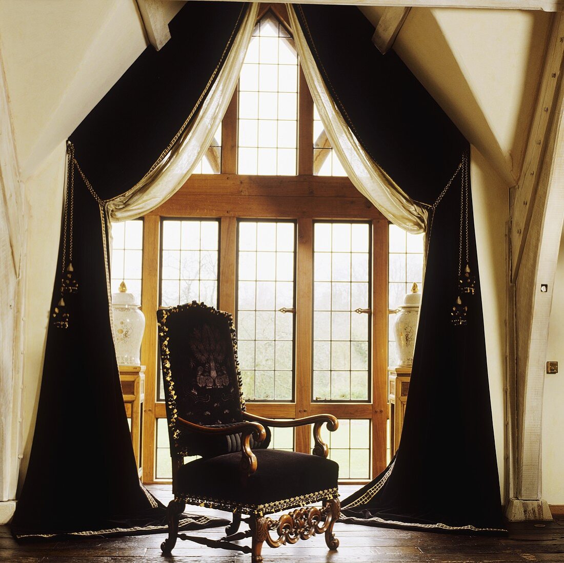 Antiker Sessel vor Fensterfront mit schwarzem Vorhang im Dachgeschoss eines Landhauses