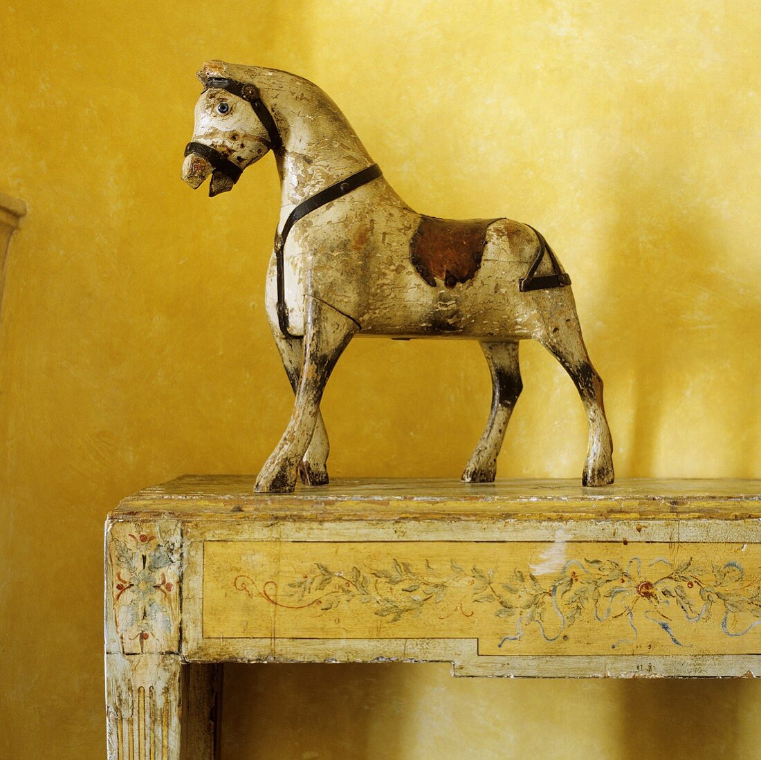 A painted wooden horse on a wooden console in front of a yellow wall