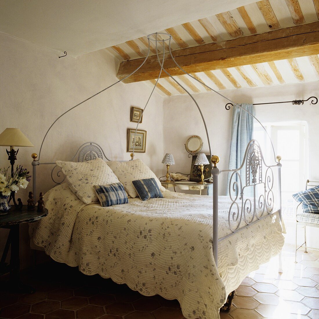 A white, antique four poster bed under and wooden beam in an attic room in a country house