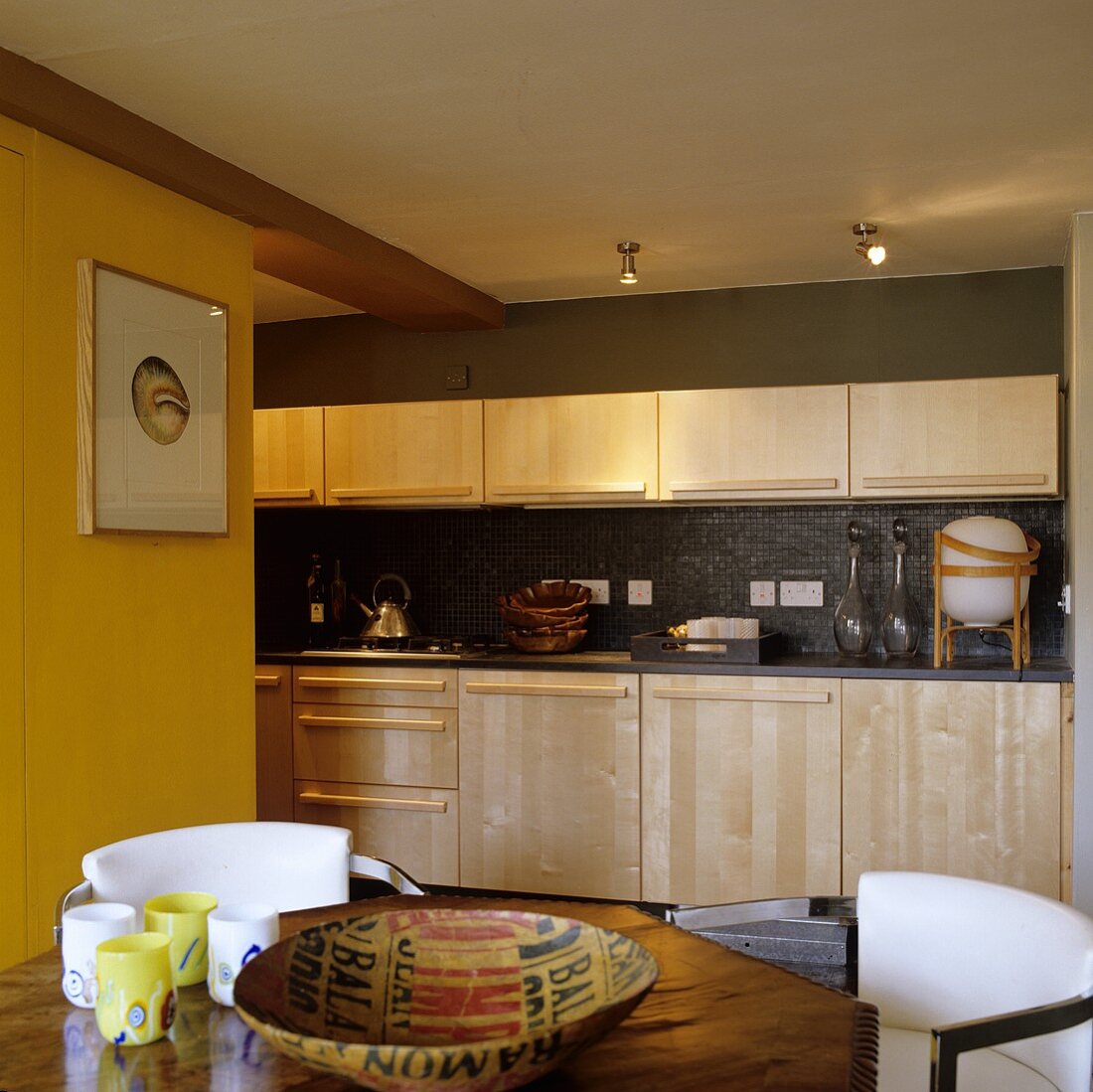 Einbauküche mit hellen Holzfronten und Holzgriffleisten vor dunkelgrauer Wand mit Deckenstrahler