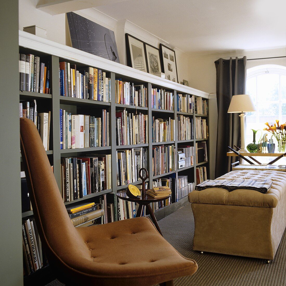 A brown leather chair in front of a grey shelf wall filled with books