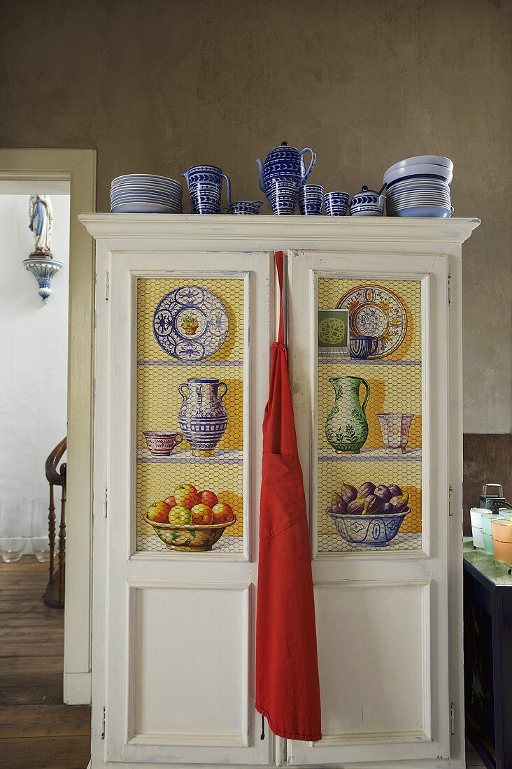 Blue crockery on a painted kitchen cupboard with a red apron hanging from the door