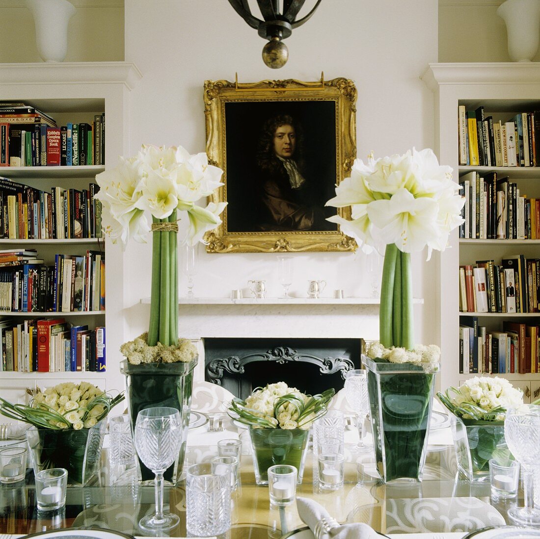 A festively decoration table with white amaryllis in a glass vase and a picture over a fireplace