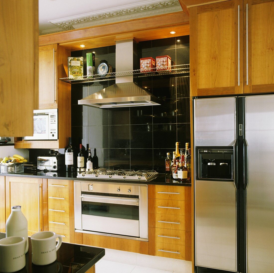 Küchenschränke mit Holzfront und integriertem Herd mit Dunstabzug vor schwarzen Wandfliesen