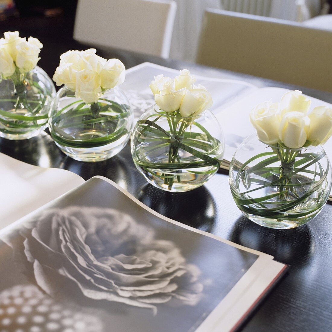 Kugelförmige Glasvasen mit weissen Rosen und offenes Buch mit Blumenmotiv