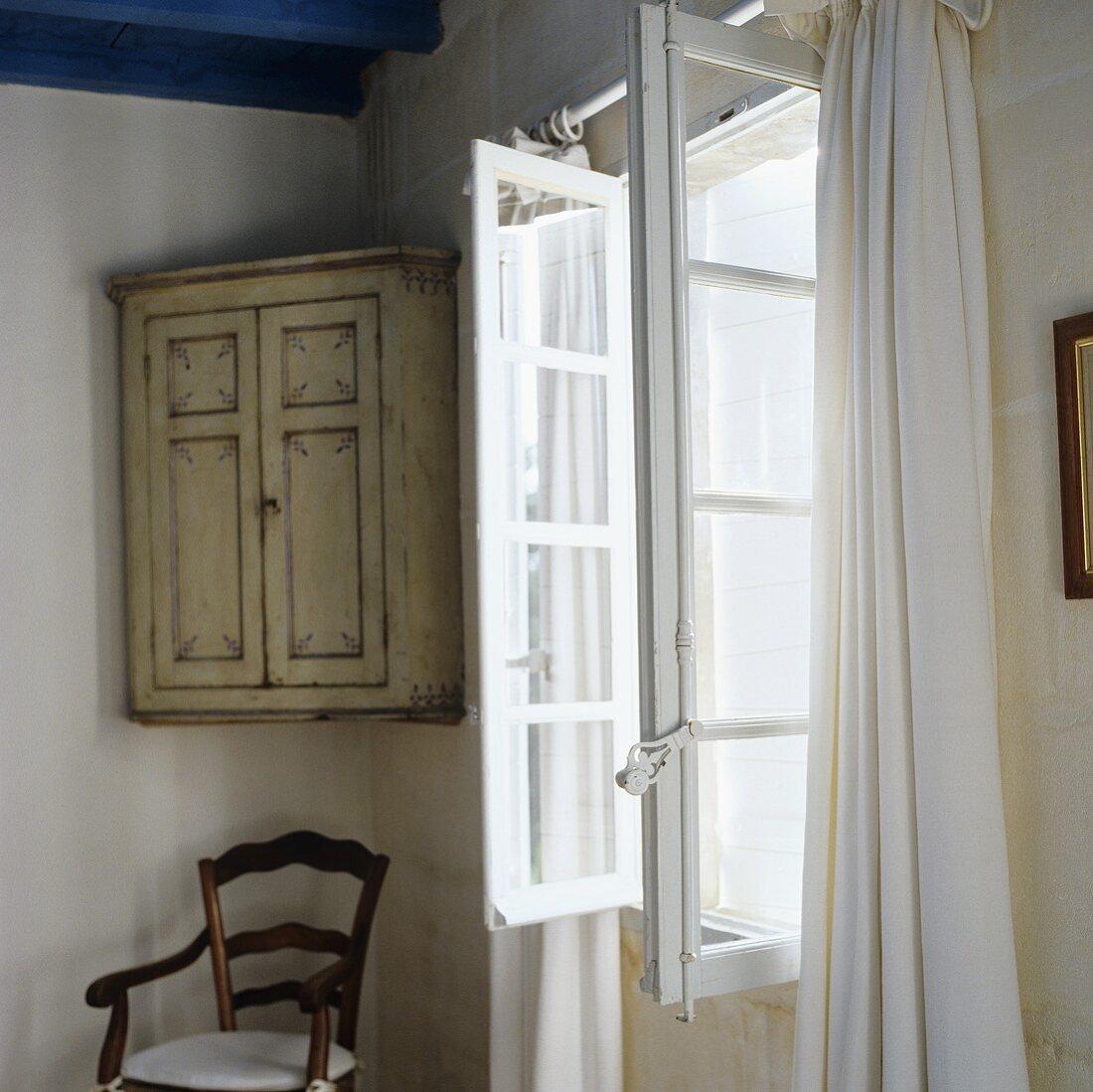 An old fashioned wall cupboard in a corner next to an open window