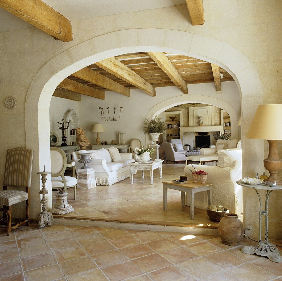 Blick durch Rundbogen in Mediterraner Wohnraum mit rustikaler Holzdecke und weiße Sofagarnitur auf Terrakottaboden