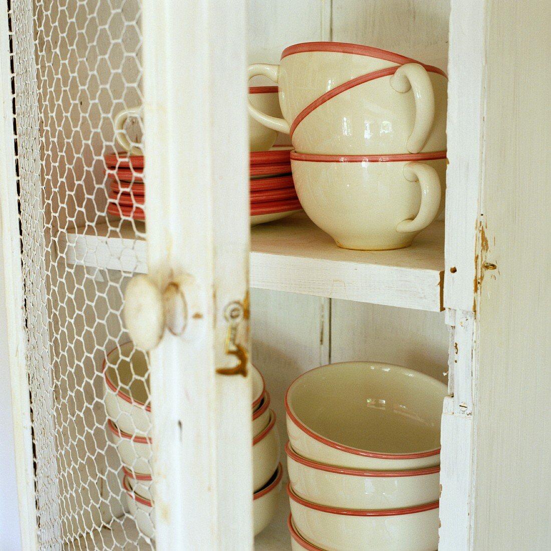 Crockery with coloured edges in a white wooden cupboard with an open door