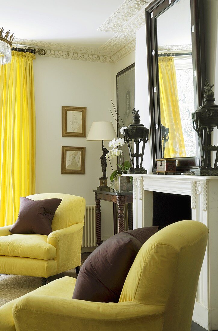 Dunkelrotes Kissen auf gelben Sesseln vor Kamin und knallgelbe Vorhänge