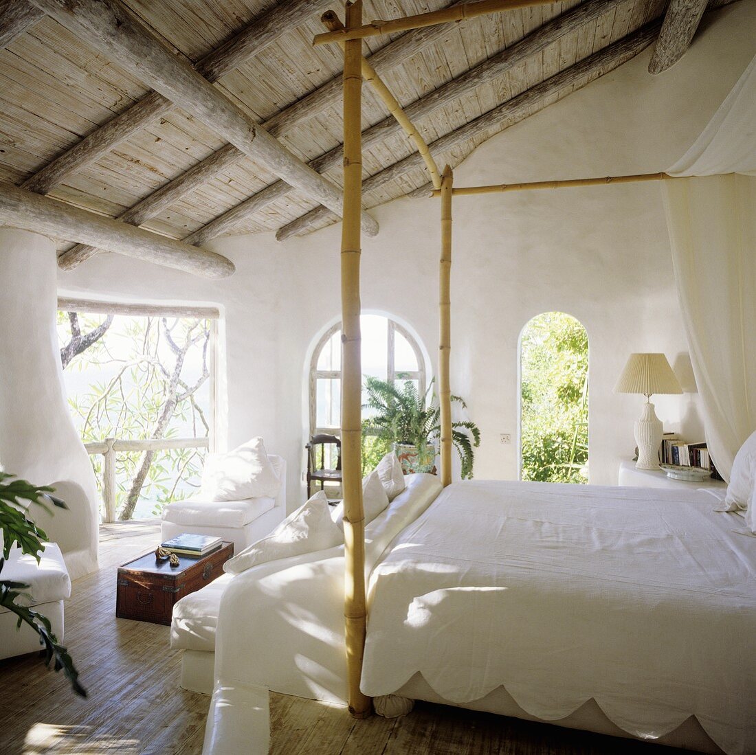 A bedroom with a rustic wooden and a white, bamboo four poster bed with a view of a garden